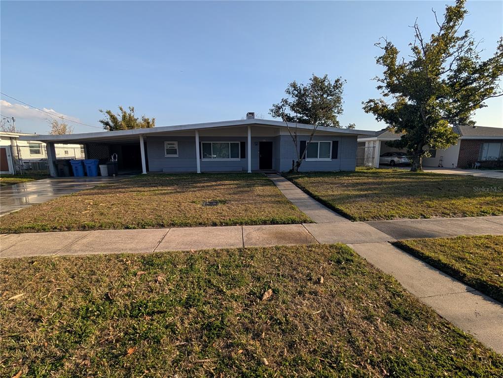 A single-story gray house with a carport and a front lawn under a clear sky — 6517 WALTON WAY, TAMPA, FL