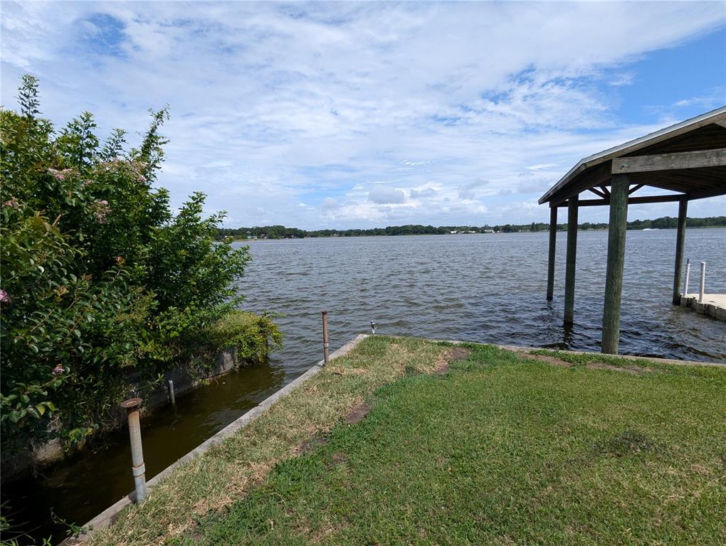A grassy yard leads to a concrete bulkhead and a covered boat dock on a lake — 6517 WALTON WAY, TAMPA, FL