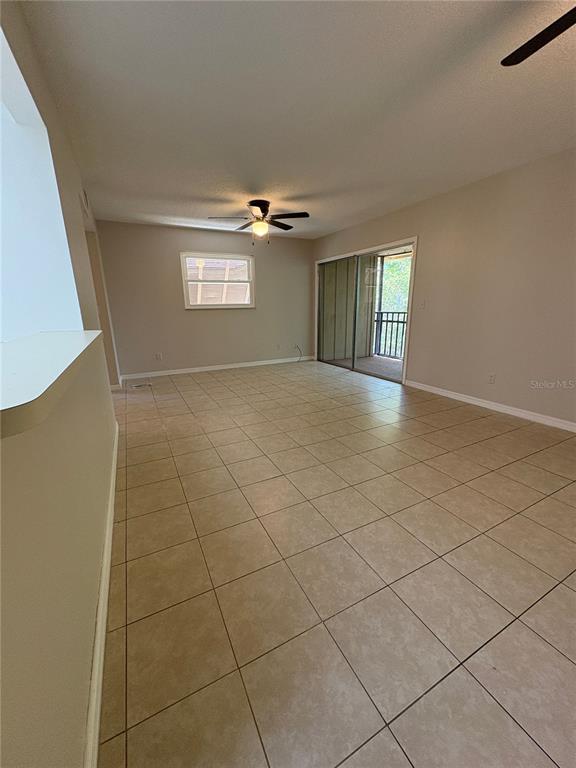 An empty living room features beige tile flooring, a ceiling fan, and a sliding glass door — 140 ORCHID WOODS COURT UNIT 7D, DELTONA, FL