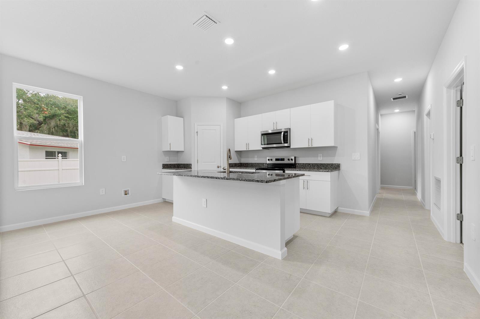 A kitchen features white cabinets, granite countertops, a central island, and light-colored tile flooring — 3344 N Park Drive, Fort Pierce FL 34982, FORT PIERCE, FL