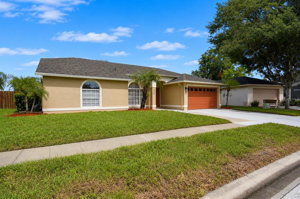 A single-story house with a tan stucco exterior, a two-car garage, and a front lawn — 2229 FOGGY RIDGE PARKWAY, LAND O LAKES, FL