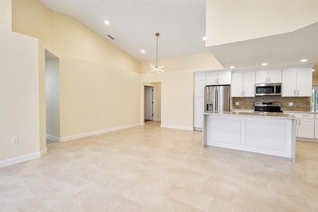 An open-concept kitchen and living area features white cabinetry, stainless steel appliances, and tile flooring — 2229 FOGGY RIDGE PARKWAY, LAND O LAKES, FL