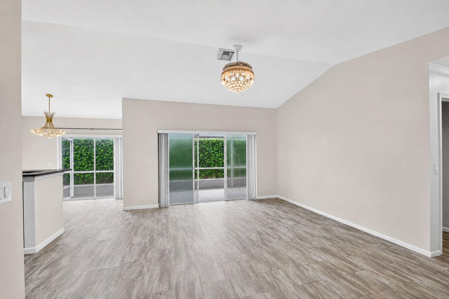 An empty living area features light wood-look tile flooring, a vaulted ceiling, and sliding doors — 208 Caribe Court, FL 33413, FL