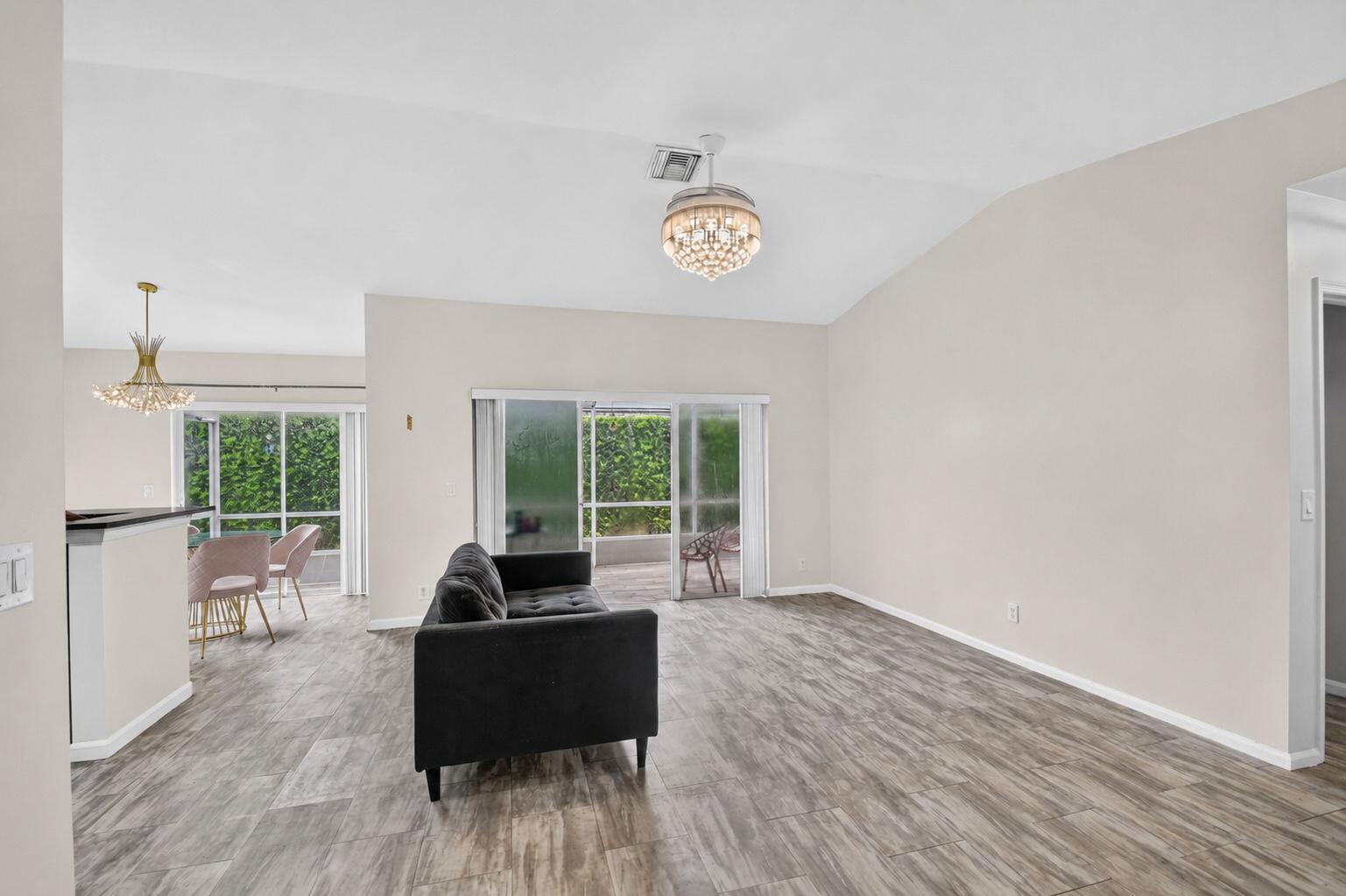 A living room features light wood-look tile flooring, a dark sofa, and a crystal chandelier — 208 Caribe Court, FL 33413, FL