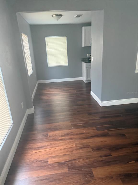 A dining area with dark wood flooring leads into a kitchen with white cabinets — 2615 E 28TH AVENUE, TAMPA, FL