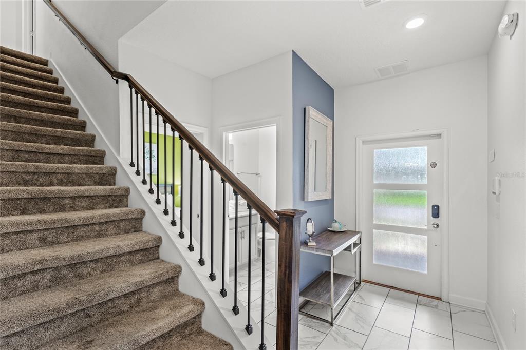 An entryway features a carpeted staircase, a blue accent wall, a console table, and tile flooring — 790 PEBBLE BEACH DRIVE, DAVENPORT, FL