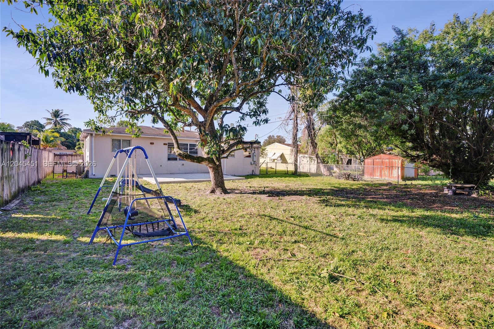 A backyard features a large tree, a blue swing set, and a small storage shed — 611 NE 171st St, North Miami Beach FL 33162, NORTH MIAMI BEACH, FL