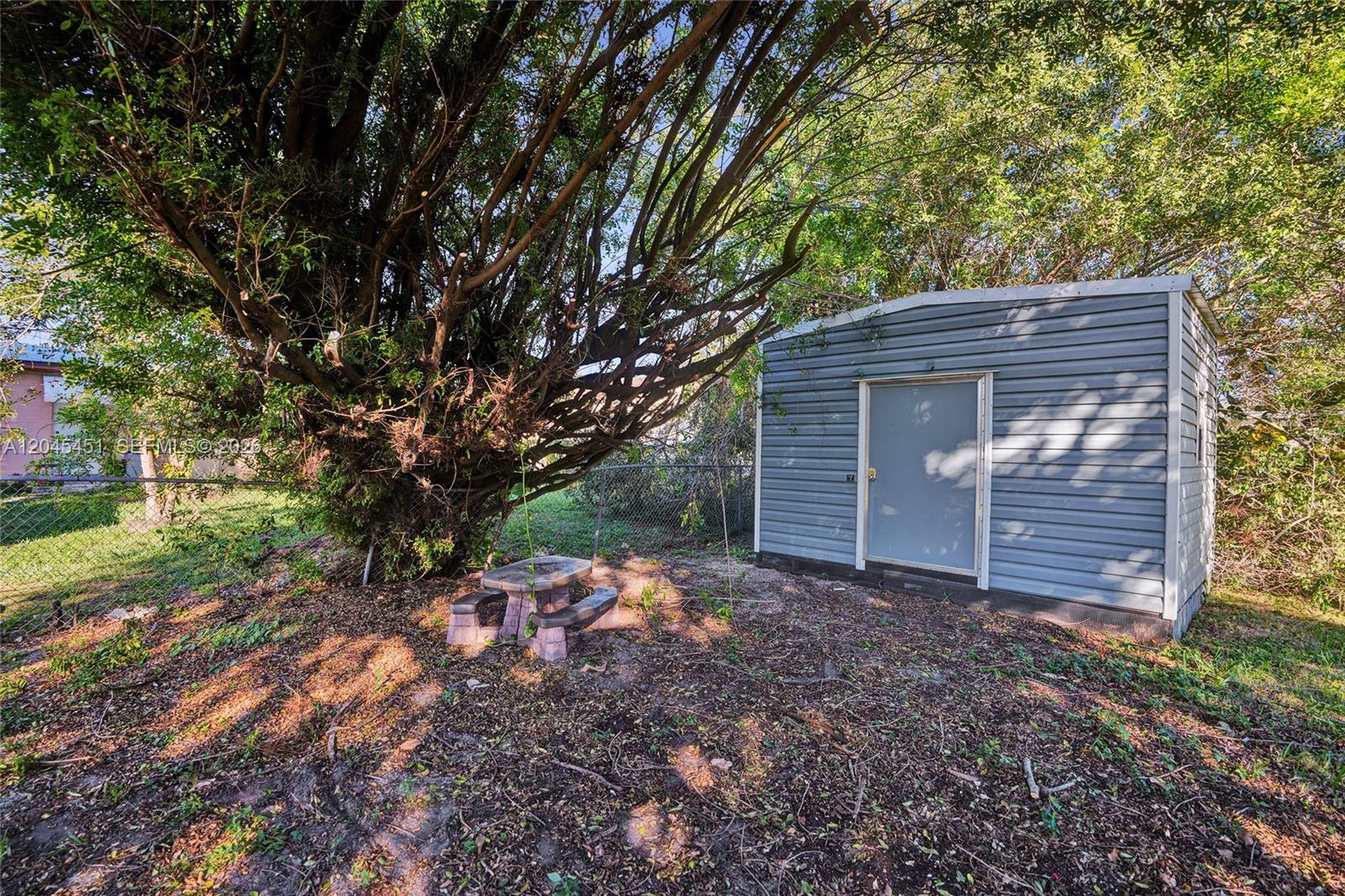 A small gray storage shed sits in a backyard next to a large tree — 611 NE 171st St, North Miami Beach FL 33162, NORTH MIAMI BEACH, FL