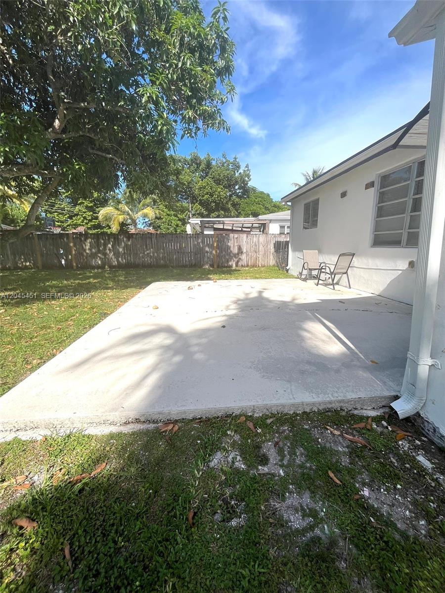 A concrete patio sits in the backyard of a house with a wooden fence — 611 NE 171st St, North Miami Beach FL 33162, NORTH MIAMI BEACH, FL