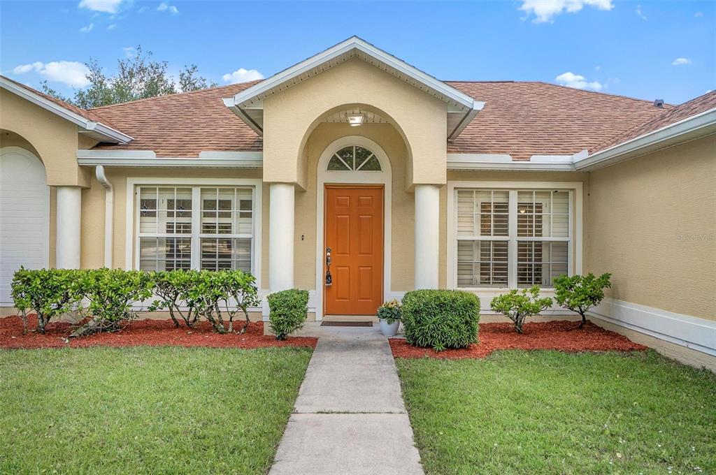 The exterior of a single-story house features a tan stucco facade, an orange front door, and a walkway — 1 ETHAN PL, PALM COAST, FL
