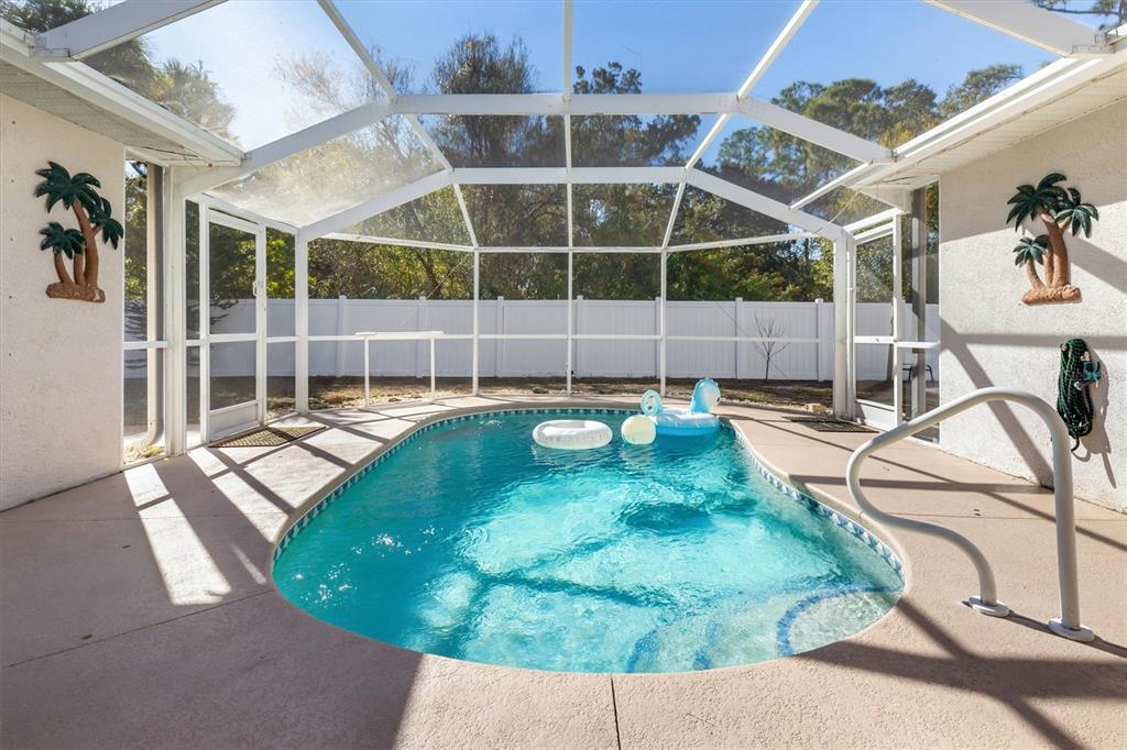 A screened-in swimming pool with a seahorse float sits in a backyard with a fence — 3707 GIBLIN DRIVE, NORTH PORT, FL