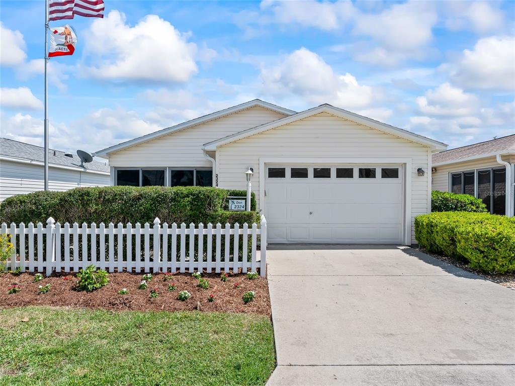 A single-story house with light siding, a white picket fence, and a concrete driveway — 2324 PICKENS PLACE, THE VILLAGES, FL