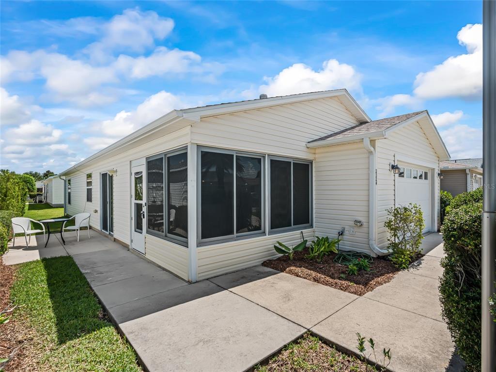 A light-colored single-story house with a screened-in porch, a concrete walkway, and a garage — 2324 PICKENS PLACE, THE VILLAGES, FL