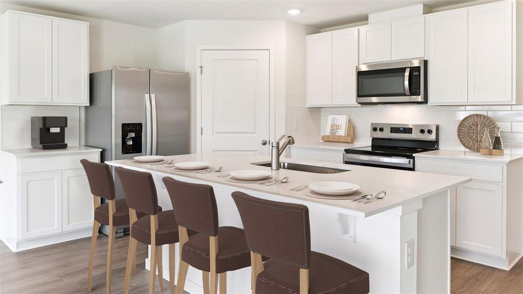 A modern kitchen features white cabinetry, stainless steel appliances, and a large central island — 1484 MORNING WALK DRIVE, ORMOND BEACH, FL