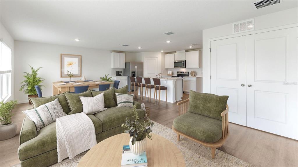 An open-concept living room features a green sofa, an armchair, and a kitchen with island seating — 1484 MORNING WALK DRIVE, ORMOND BEACH, FL