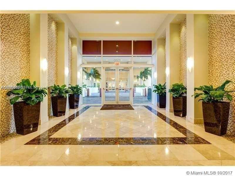 A bright building lobby features marble floors, decorative wall tiles, and four large potted plants — 7350 SW 89th St # 1707S, Miami FL 33156, MIAMI, FL