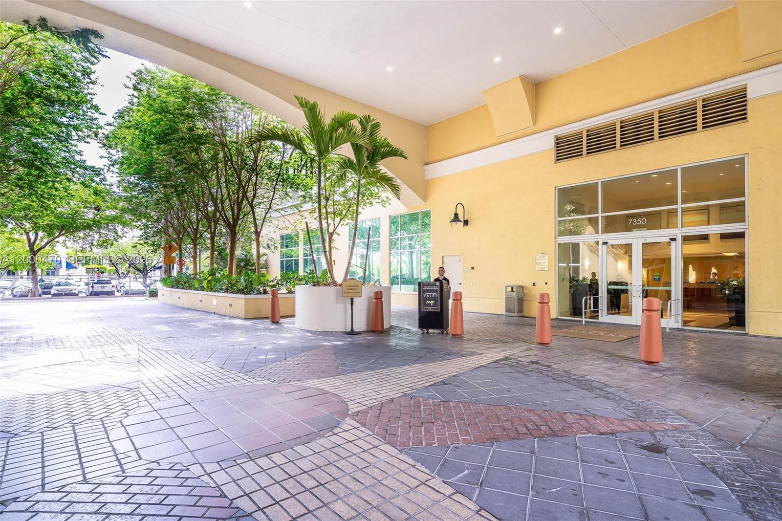 The exterior entrance of a building features a covered driveway, valet stand, and paved walkway — 7350 SW 89th St # 1707S, Miami FL 33156, MIAMI, FL