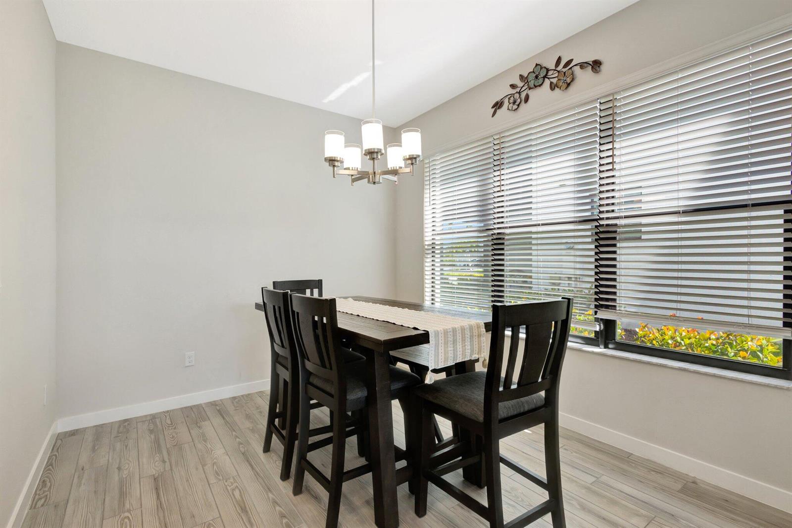 A dining room features a dark wood table with chairs, a chandelier, and window blinds — 8654 Antarus Drive, Lake Worth FL 33467, LAKE WORTH, FL