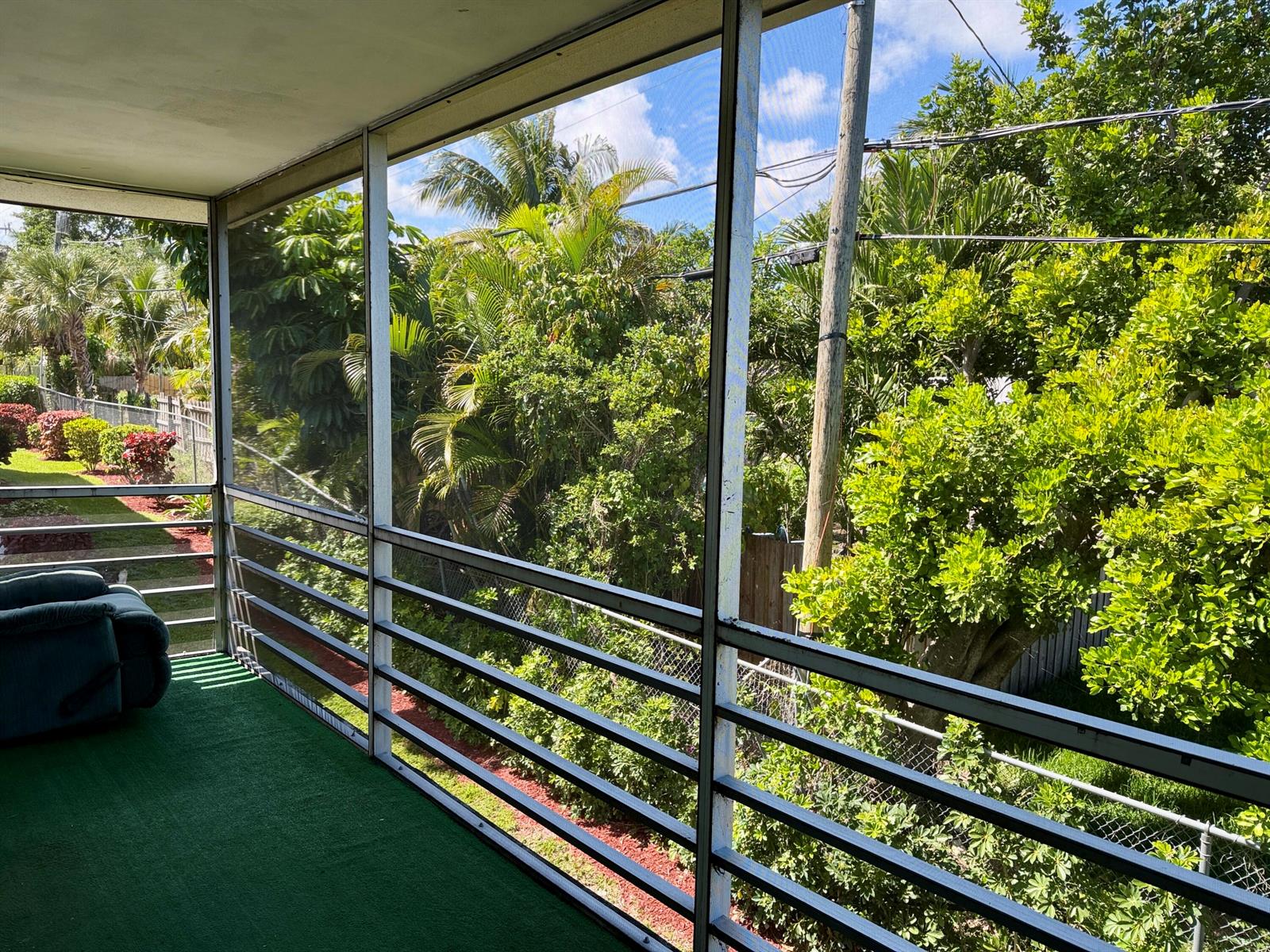 A screened-in balcony with green outdoor carpeting overlooks a lush, tree-filled backyard — 3402 Cynthia Lane # 205, FL 33461, FL