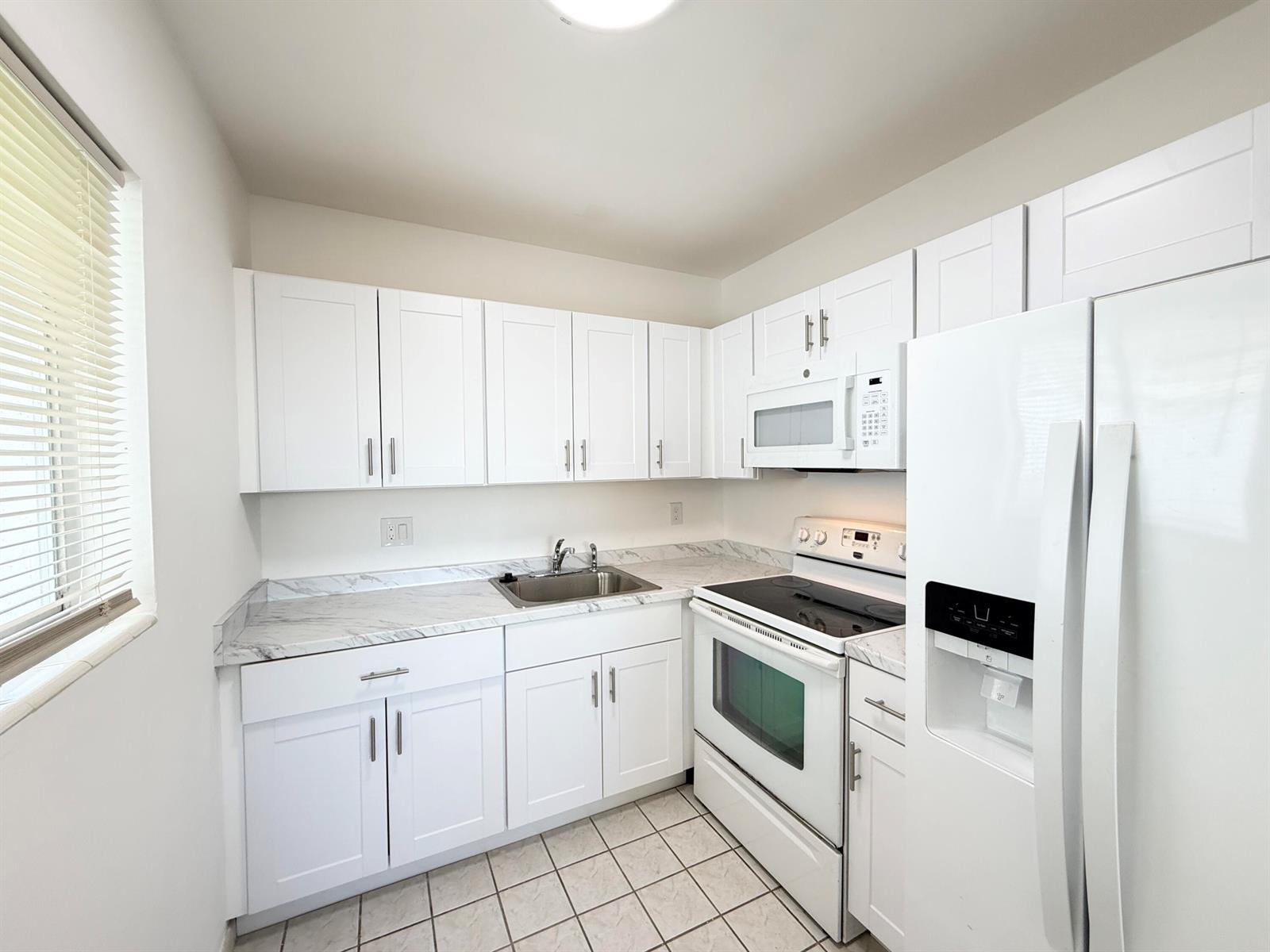 A kitchen features white cabinets, marble-patterned countertops, white appliances, and light-colored tile flooring — 3402 Cynthia Lane # 205, FL 33461, FL