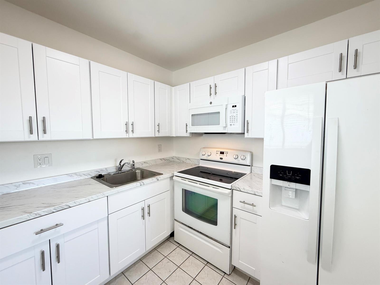 A kitchen features white cabinets, white appliances, and marble-patterned countertops over a tiled floor — 3402 Cynthia Lane # 205, FL 33461, FL