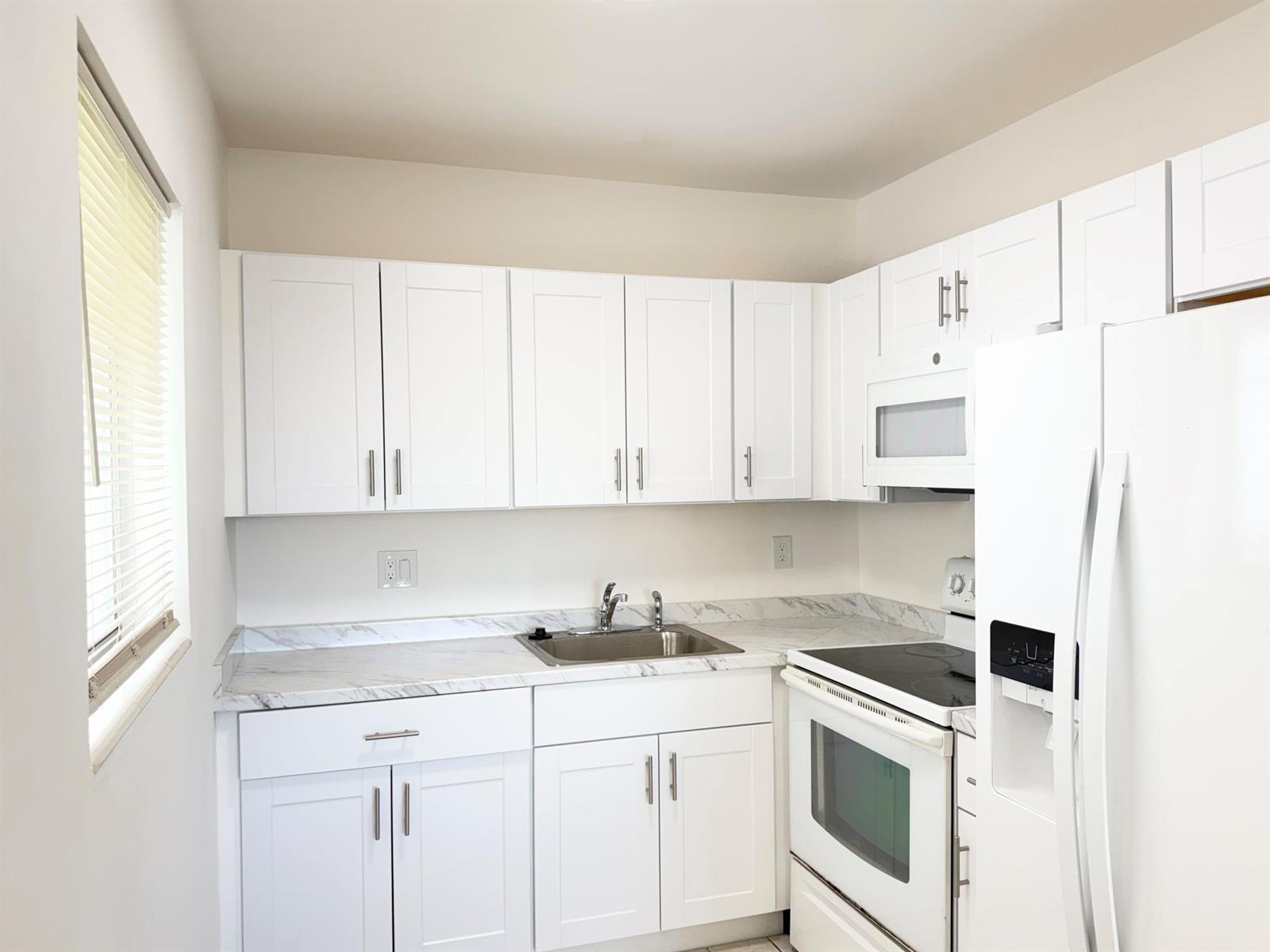 A kitchen features white shaker cabinets, marble-look countertops, and white appliances — 3402 Cynthia Lane # 205, FL 33461, FL