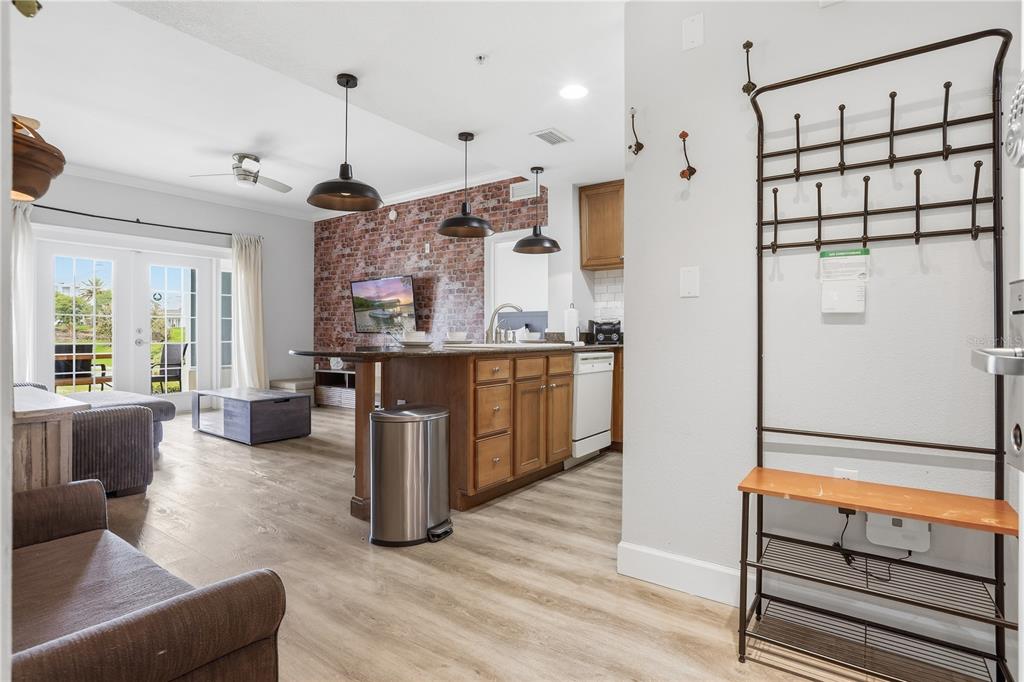An open-concept living area features a brick accent wall, kitchen island, and a metal coat rack — 7673 HERITAGE CROSSING WAY UNIT 102, REUNION, FL