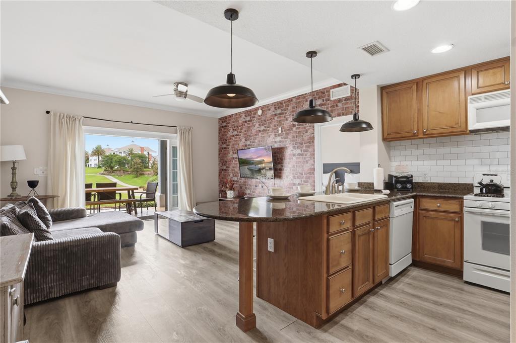 An open-concept kitchen and living area features a brick accent wall and a patio view — 7673 HERITAGE CROSSING WAY UNIT 102, REUNION, FL