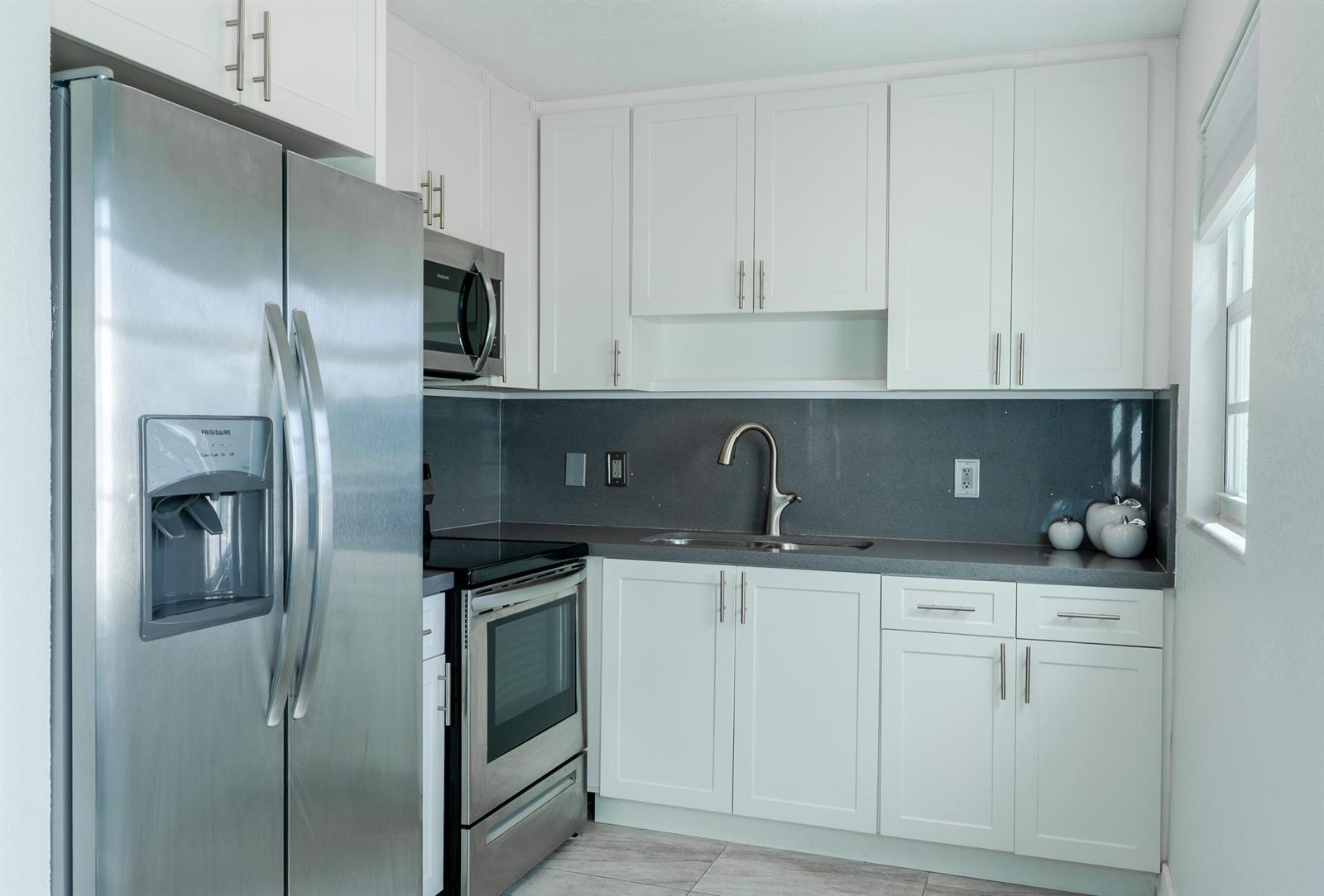 A kitchen features white cabinets, stainless steel appliances, and a dark gray countertop — 592 Fanshaw O, Boca Raton FL 33434, BOCA RATON, FL