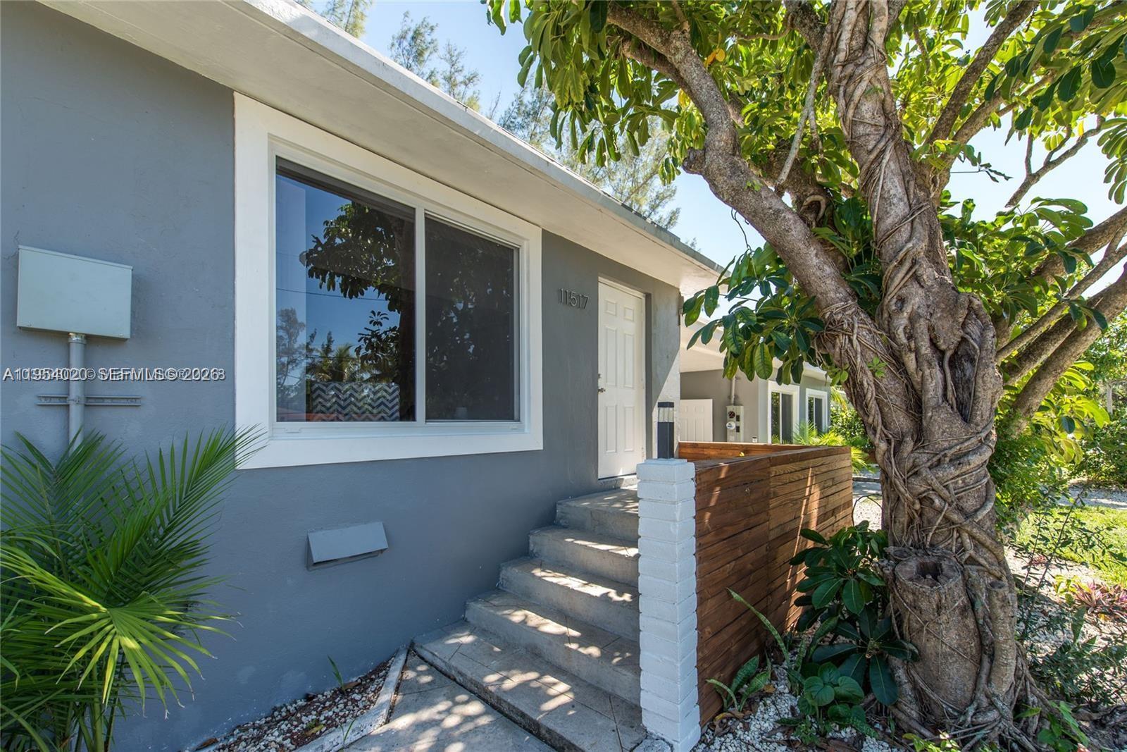 A gray house exterior features a white-trimmed window, concrete steps, and a wooden privacy screen — 11515 NE 12th Ave, Miami FL 33161, MIAMI, FL