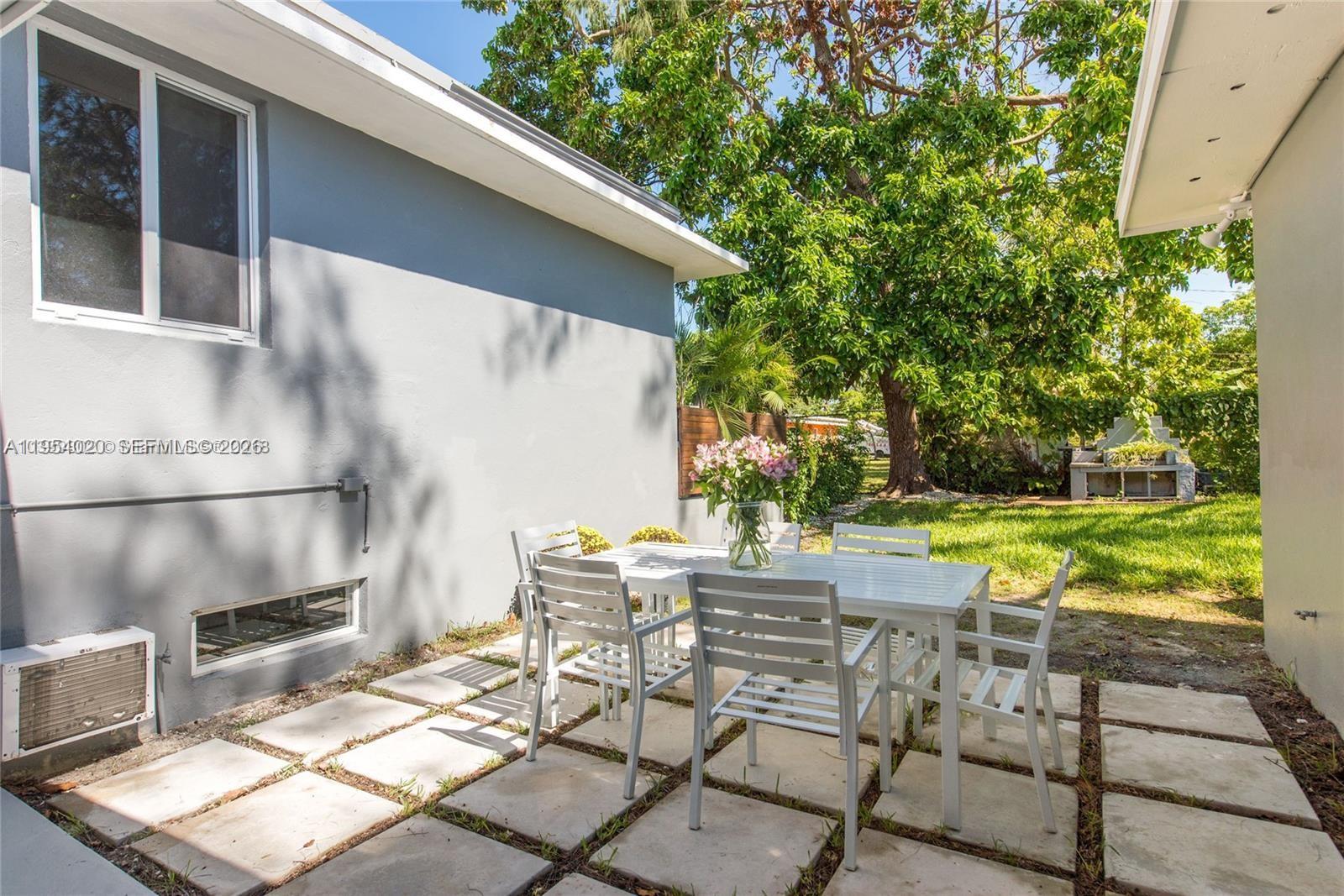A white patio set sits on a paved stone area beside a gray house exterior — 11515 NE 12th Ave, Miami FL 33161, MIAMI, FL