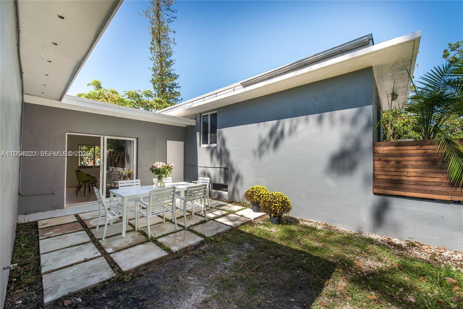 A gray exterior wall features a patio with a white dining set and pavers — 11515 NE 12th Ave, Miami FL 33161, MIAMI, FL