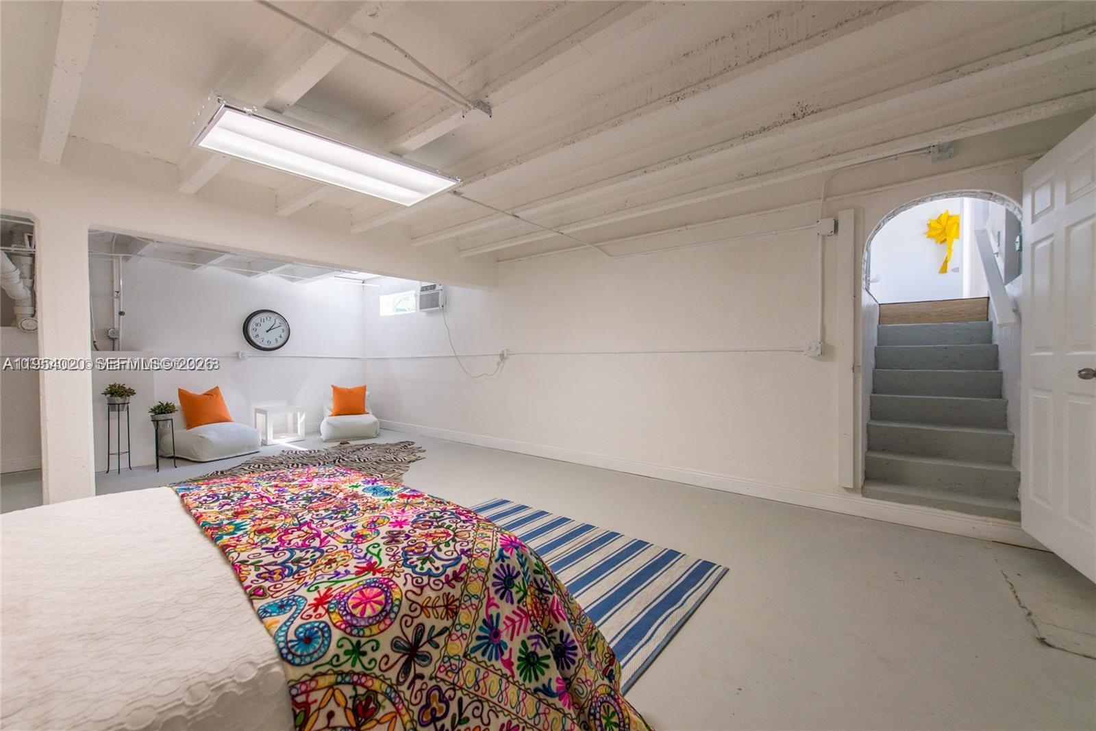 A basement bedroom features white-painted exposed ceiling beams, concrete floors, and a staircase entry — 11515 NE 12th Ave, Miami FL 33161, MIAMI, FL