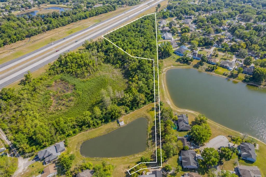 An aerial view shows a wooded lot outlined in white next to a residential pond — SEAFARER WAY, ORLANDO, FL
