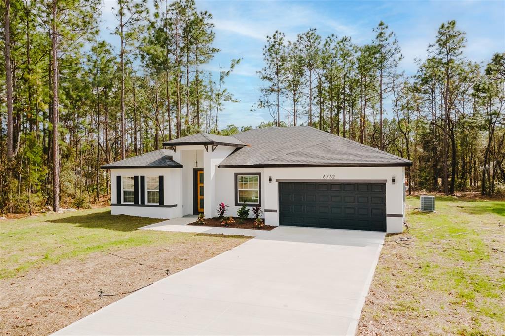 A single-story white house with a dark garage door and a concrete driveway — 6732 SW 132ND STREET, OCALA, FL