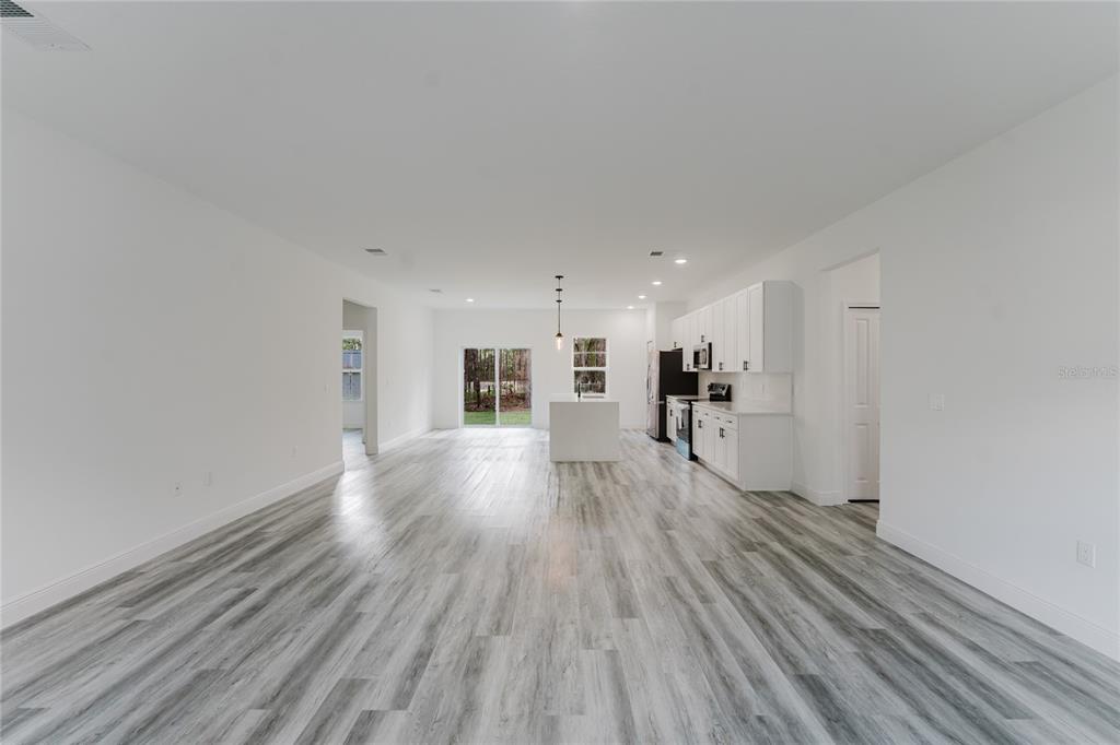 An open-concept kitchen and living area features white cabinetry, a center island, and wood-look flooring — 6732 SW 132ND STREET, OCALA, FL