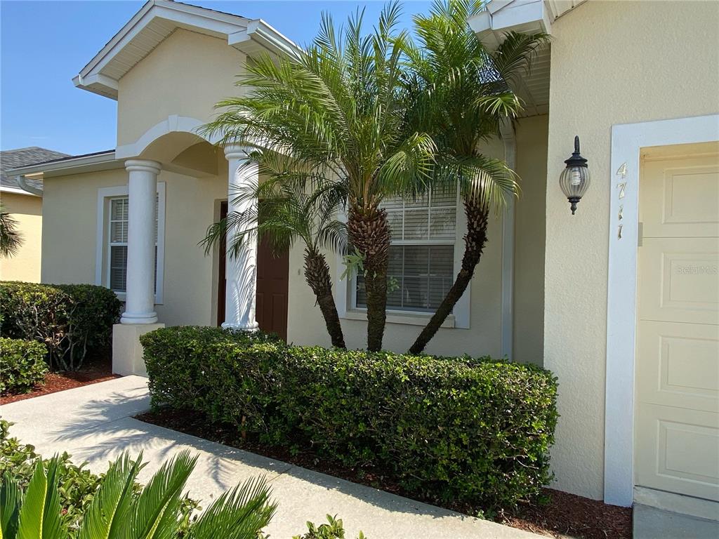 The exterior of a house features a palm tree, a hedge, and a garage door — 4711 MANDOLIN LOOP, WINTER HAVEN, FL