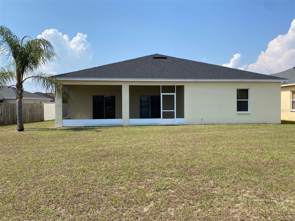The rear exterior of a single-story house features a screened-in lanai and a grassy yard — 4711 MANDOLIN LOOP, WINTER HAVEN, FL