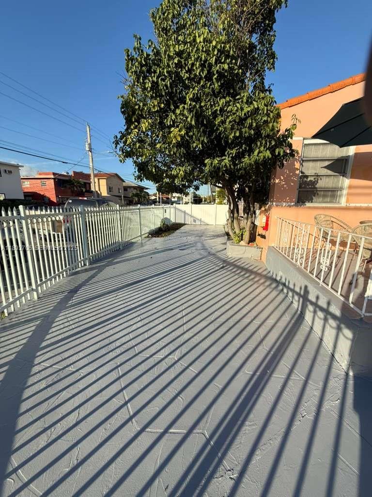 A paved side yard features a large tree, white metal fencing, and a peach-colored house — 300 NW 13th Ave, Miami FL 33125, MIAMI, FL