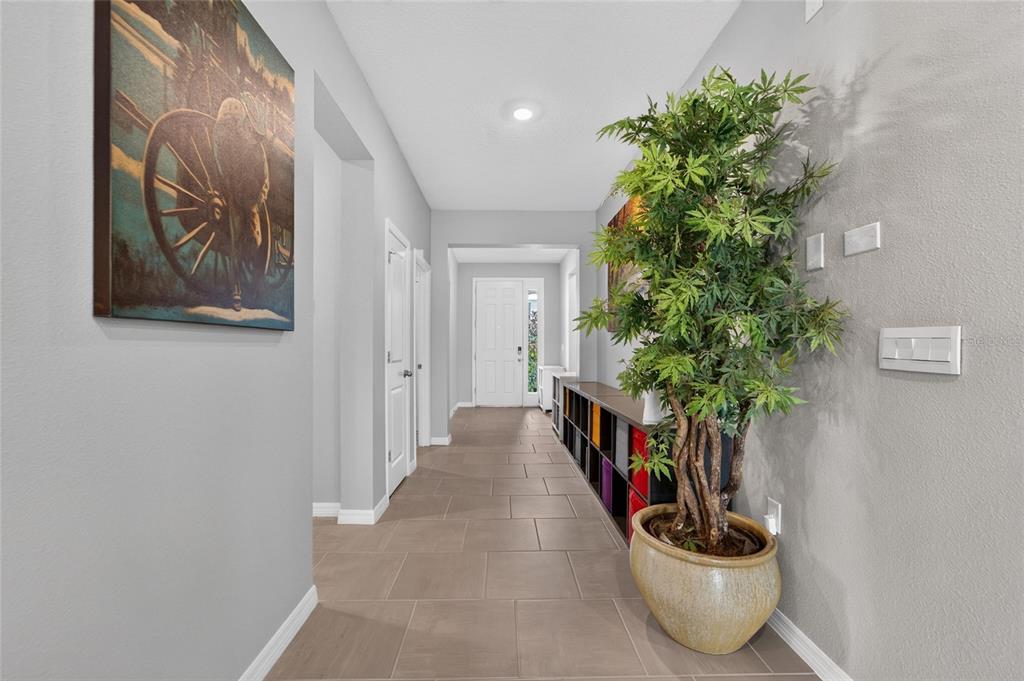 A hallway with light gray walls, tile flooring, a large potted plant, and wall art — 10675 TALLY FAWN LOOP, SAN ANTONIO, FL