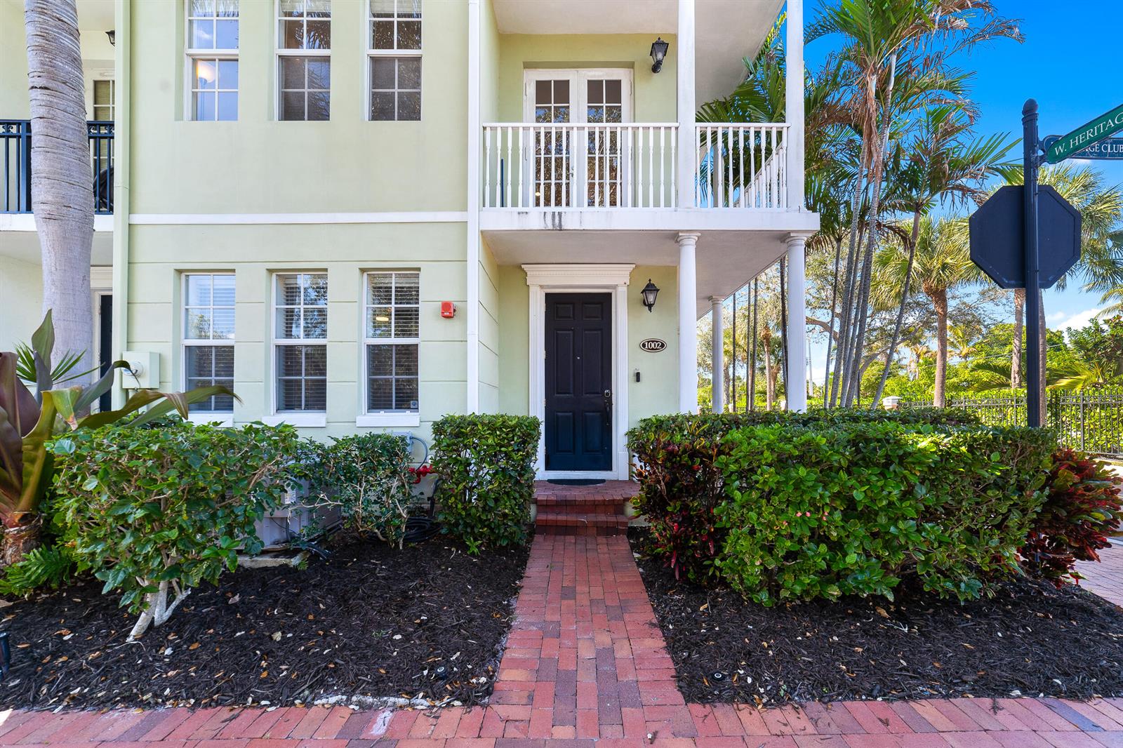 A two-story light green townhouse features a black front door and a second-floor balcony — 1002 E Heritage Club Circle, Delray Beach FL 33483, DELRAY BEACH, FL