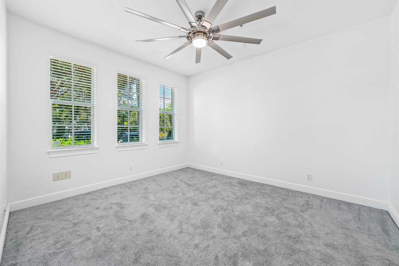An empty bedroom features white walls, gray carpeting, three windows, and a ceiling fan — 1002 E Heritage Club Circle, Delray Beach FL 33483, DELRAY BEACH, FL
