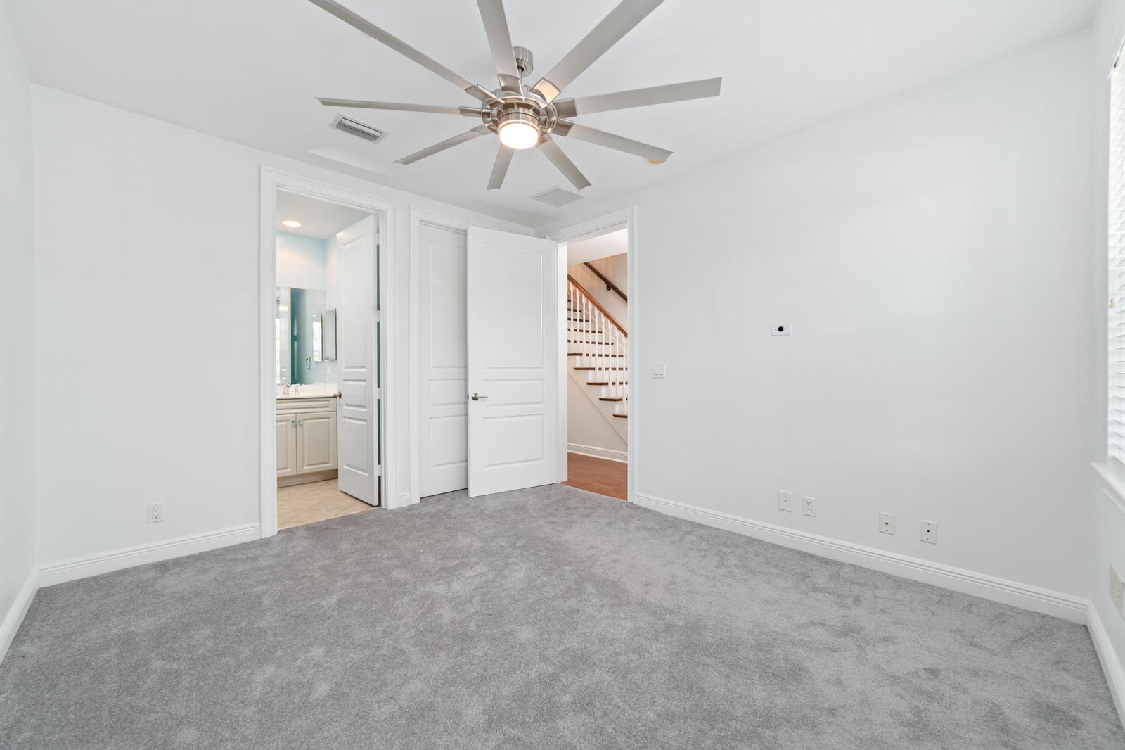 A bedroom with gray carpet, white walls, a ceiling fan, and two open doorways — 1002 E Heritage Club Circle, Delray Beach FL 33483, DELRAY BEACH, FL