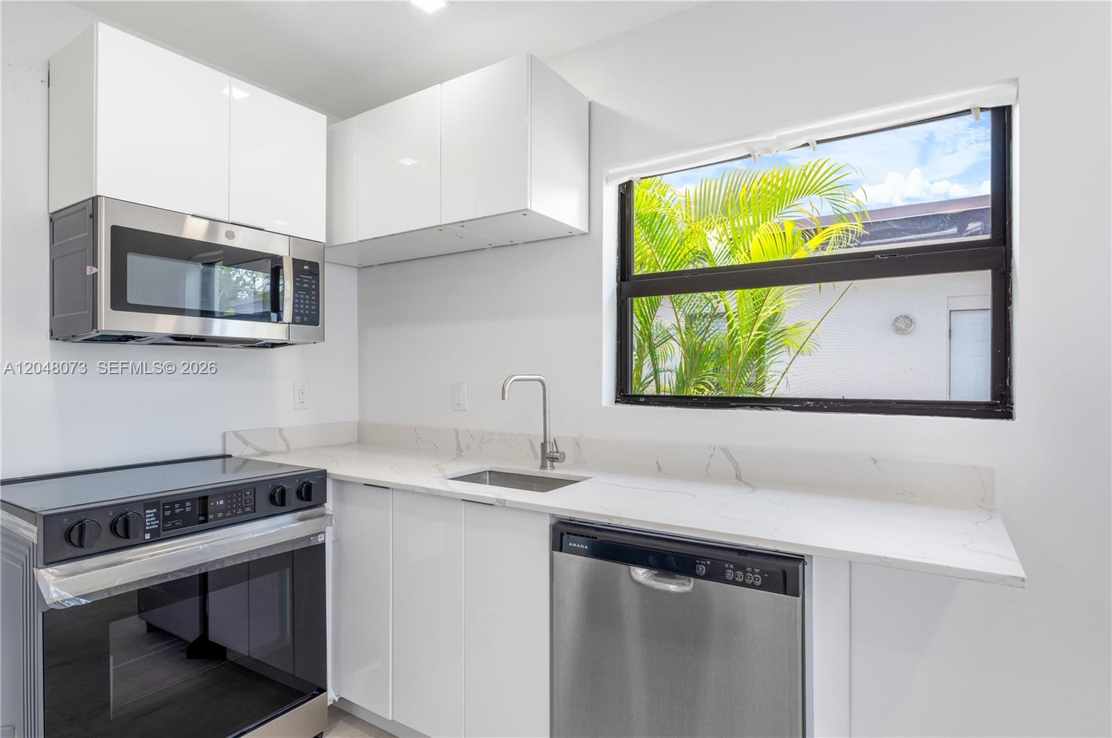 A modern kitchen features white cabinets, stainless steel appliances, and a window with palm trees — 551 NE 26th St # 1, Wilton Manors FL 33305, WILTON MANORS, FL