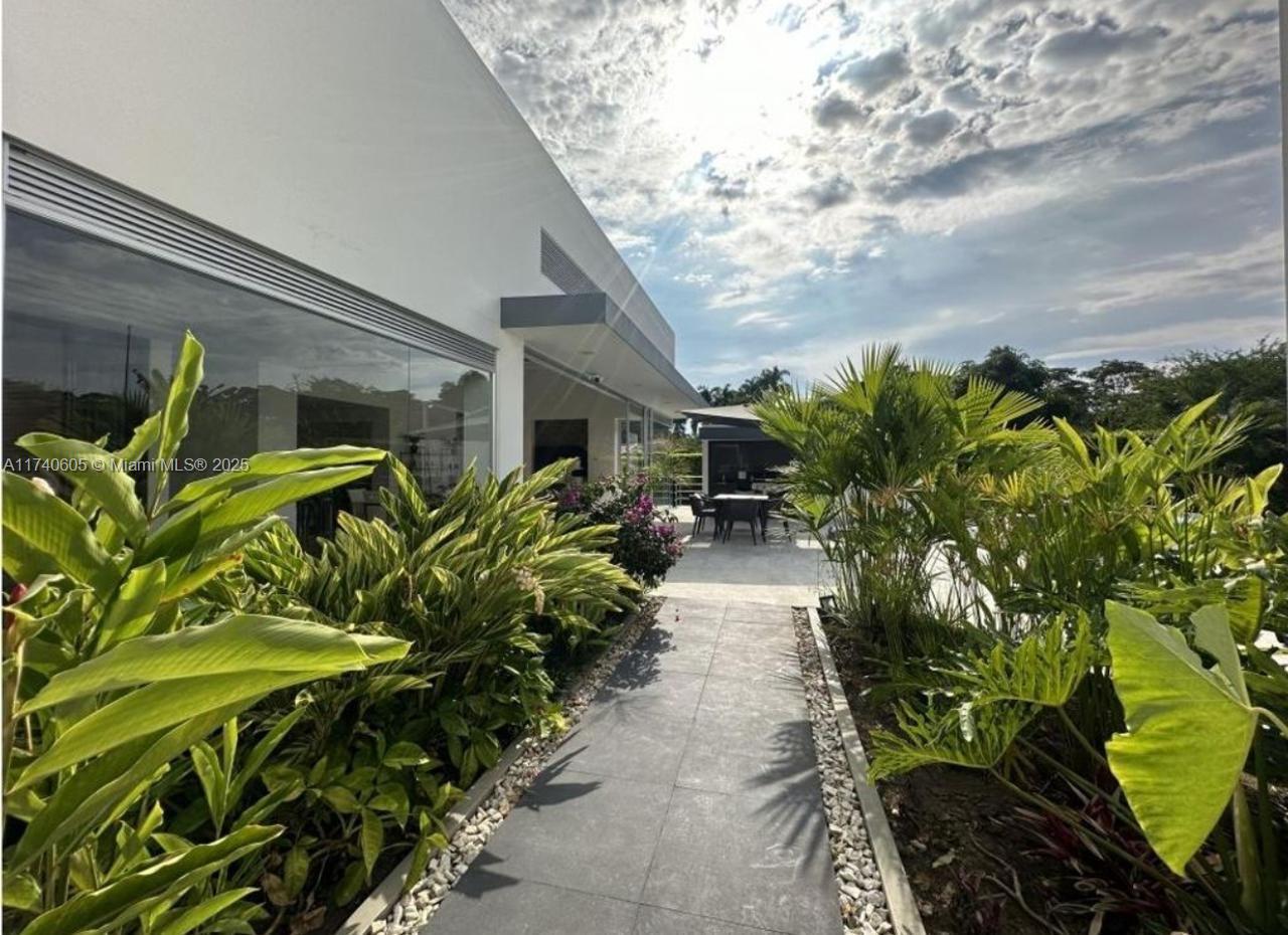 A stone walkway leads past lush tropical landscaping toward a modern patio and outdoor dining area — OTHER COUNTRY - NOT IN USA, PP