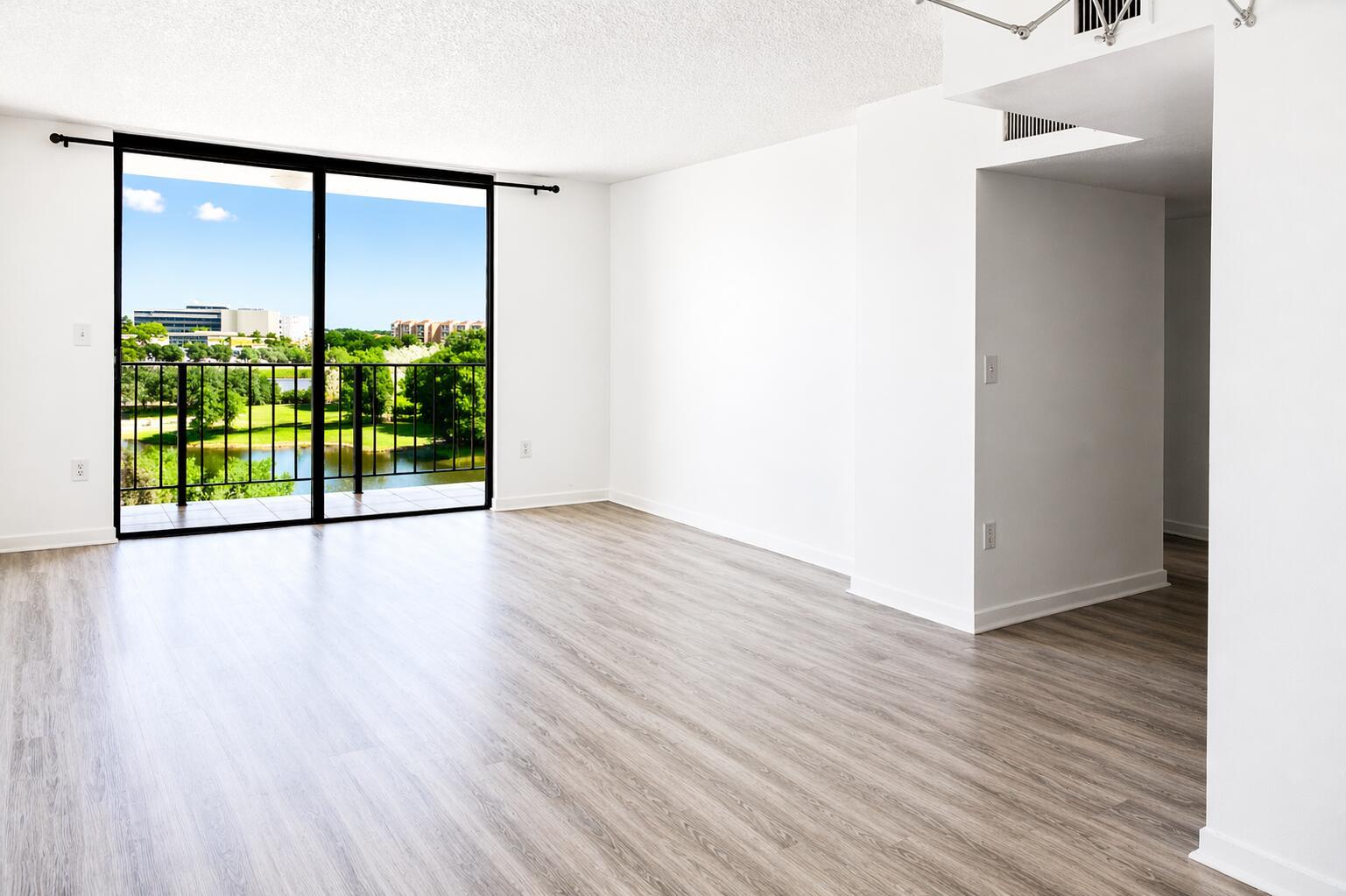 An empty living room with light wood-look flooring, white walls, and a balcony overlooking water — 9682 Fontainebleau Boulevard # 603, Miami FL 33172, MIAMI, FL