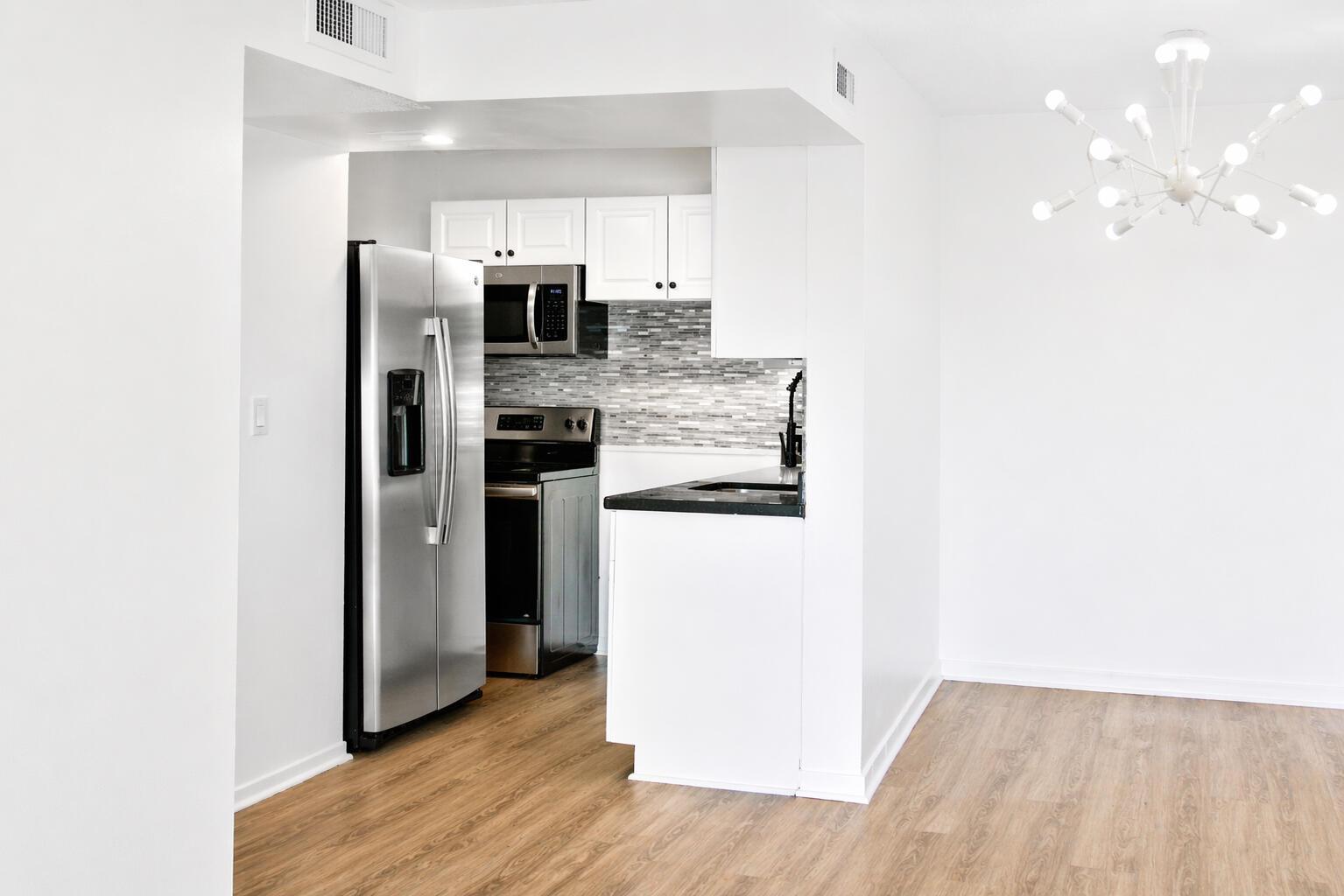 A kitchen with stainless steel appliances, white cabinets, and a tiled backsplash opens to a room — 9682 Fontainebleau Boulevard # 603, Miami FL 33172, MIAMI, FL