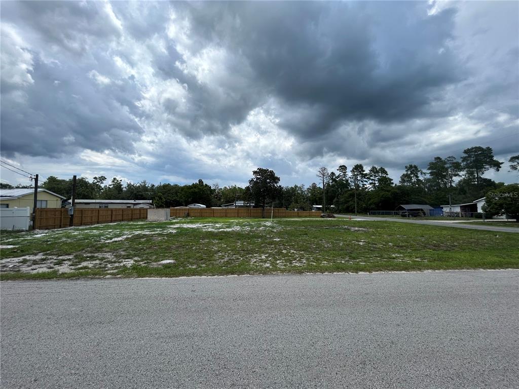 A vacant, grassy residential lot sits under a cloudy sky next to a wooden fence — 28245 BOUGAINVILLEA AVENUE, PAISLEY, FL