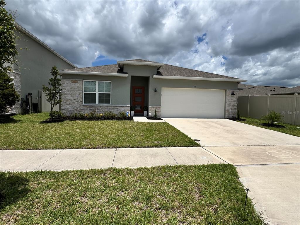 A single-story house with a stone facade, a red front door, and a two-car garage — 415 TALISI LOOP, ST CLOUD, FL