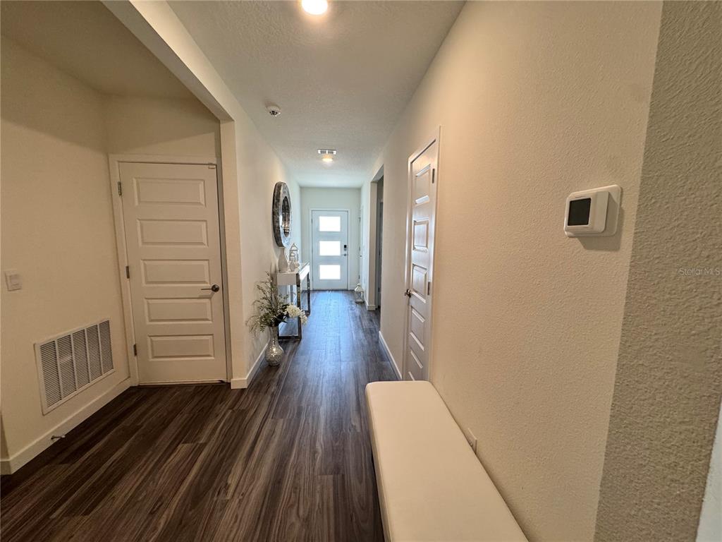 A bright hallway features wood-look flooring, a white bench, and a front door with windows — 415 TALISI LOOP, ST CLOUD, FL
